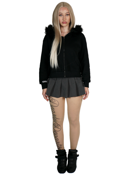 Person wearing a black hoodie with fur trim, black skirt, and black boots on a white background