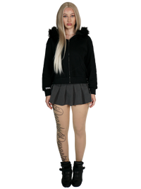 Person wearing a black hoodie with fur trim, black skirt, and black boots on a white background