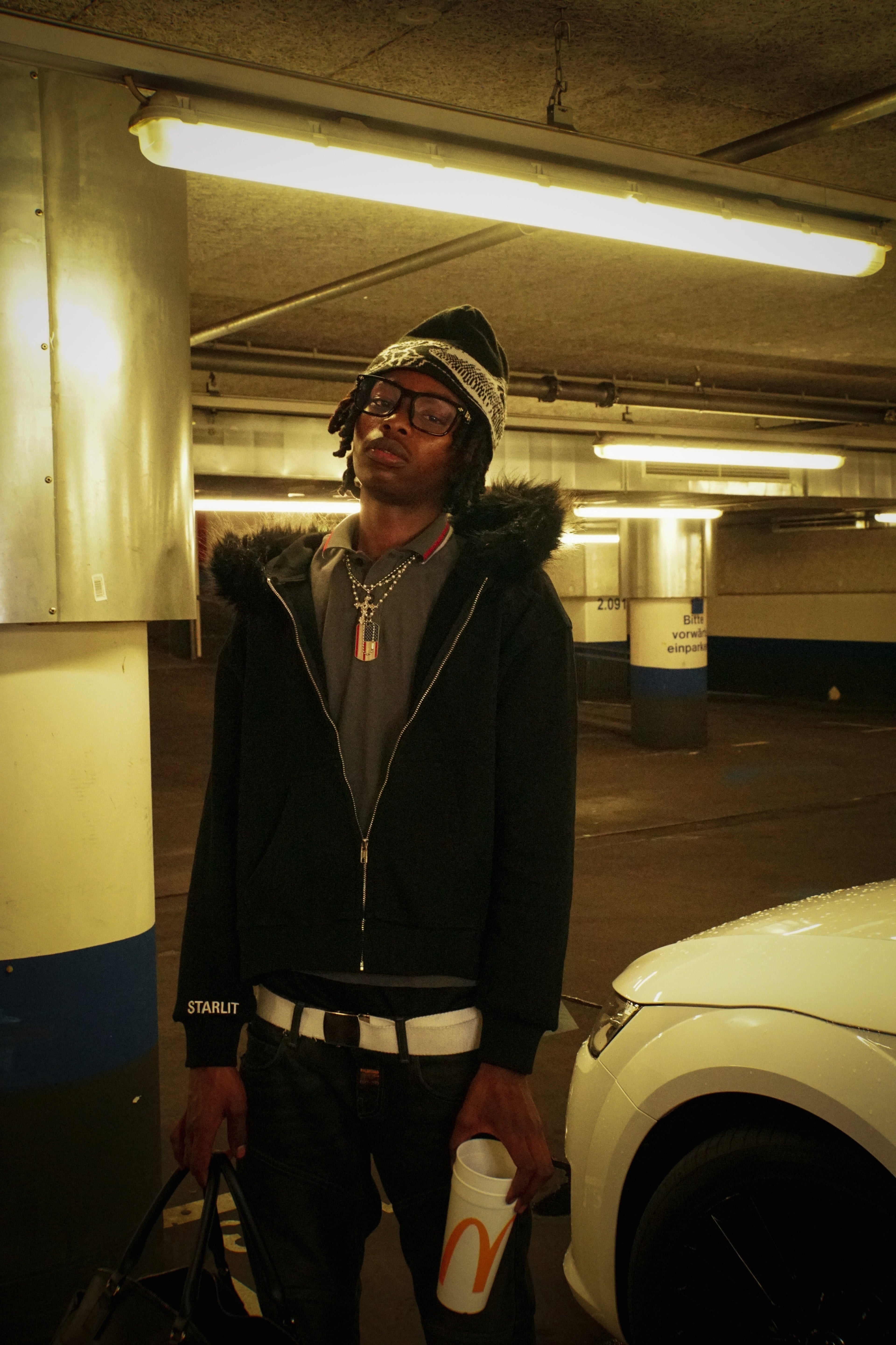 Model in Fur-Zip Hoodie, Standing in Parking Garage with Cup