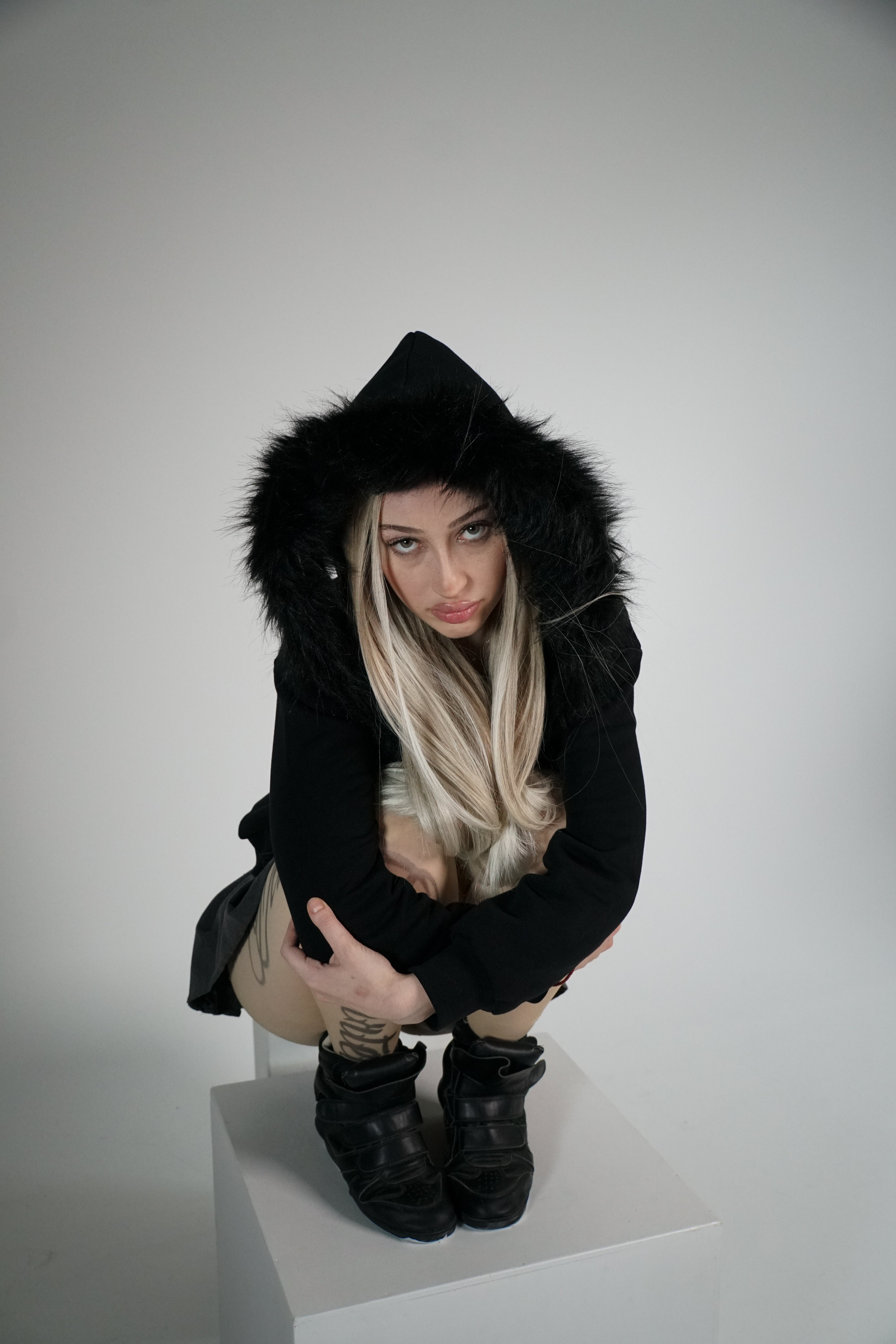 Person wearing a black fur-lined coat on a white background