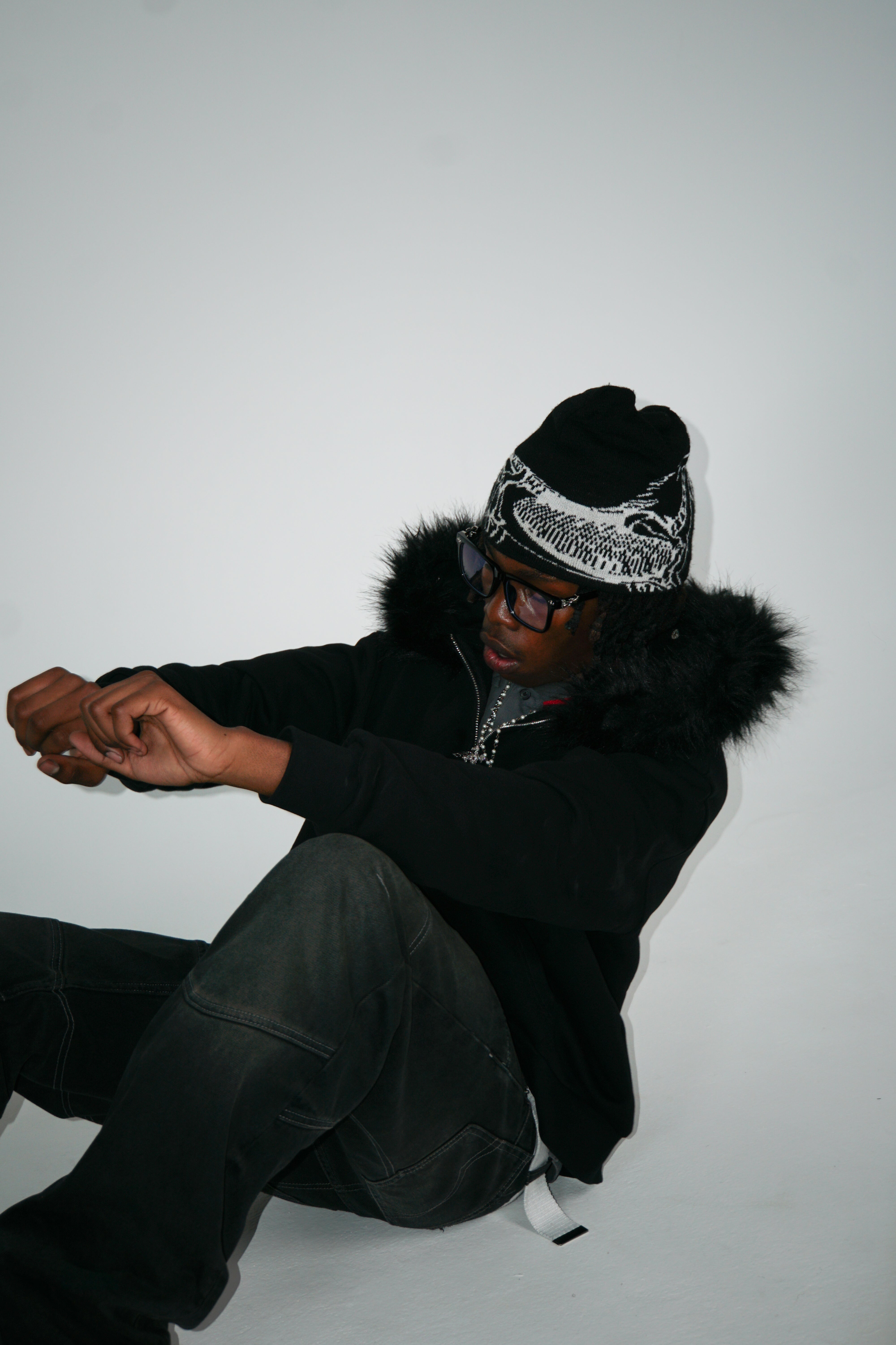 Person wearing a black coat with fur trim and a patterned hat on a white background