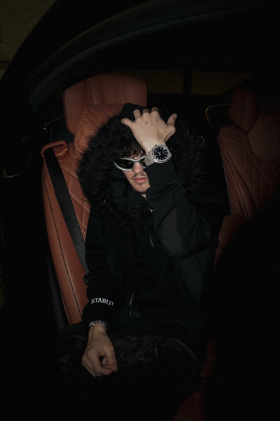Person sitting inside a mercedes s class wearing sunglasses and a black outfit with 'STARLIT' text.