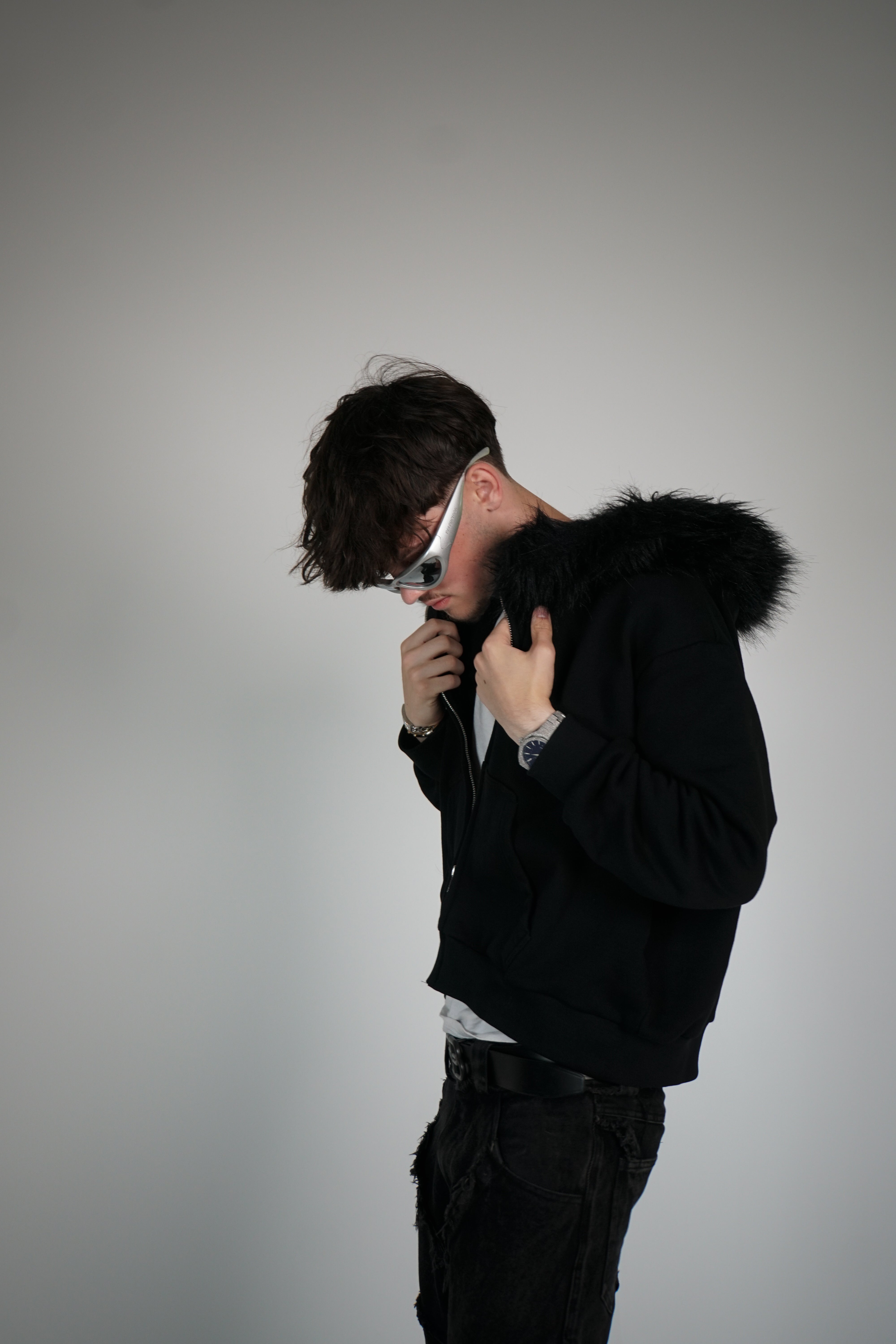 Person wearing a black jacket with fur hood against a gray background
