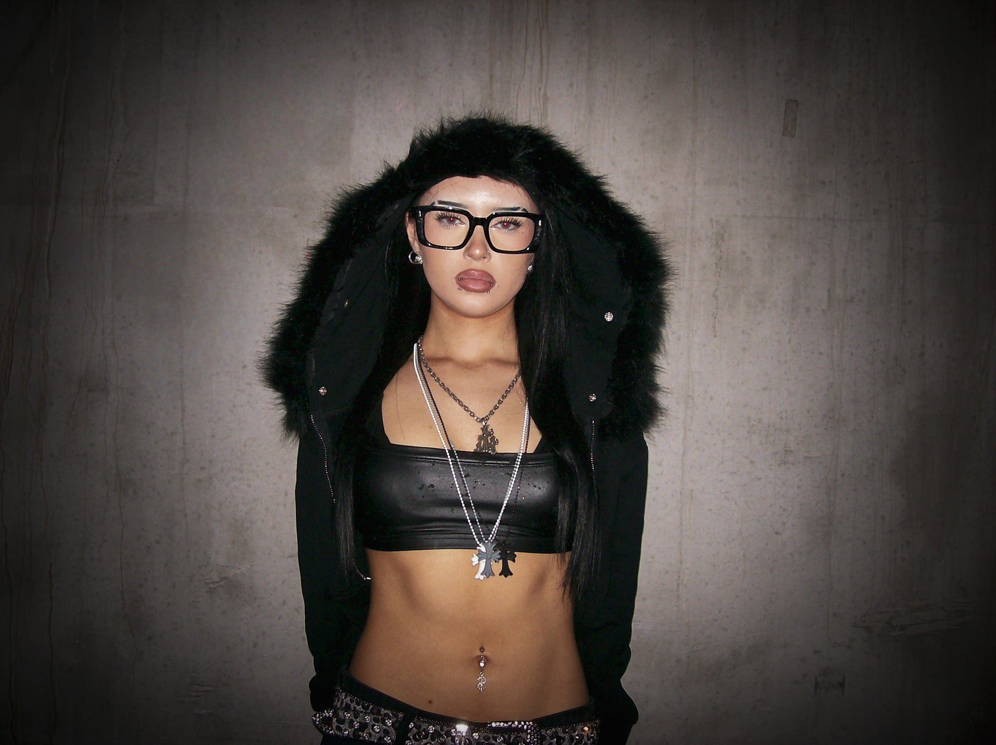 Person wearing a black fur-lined coat and black top against a gray background
