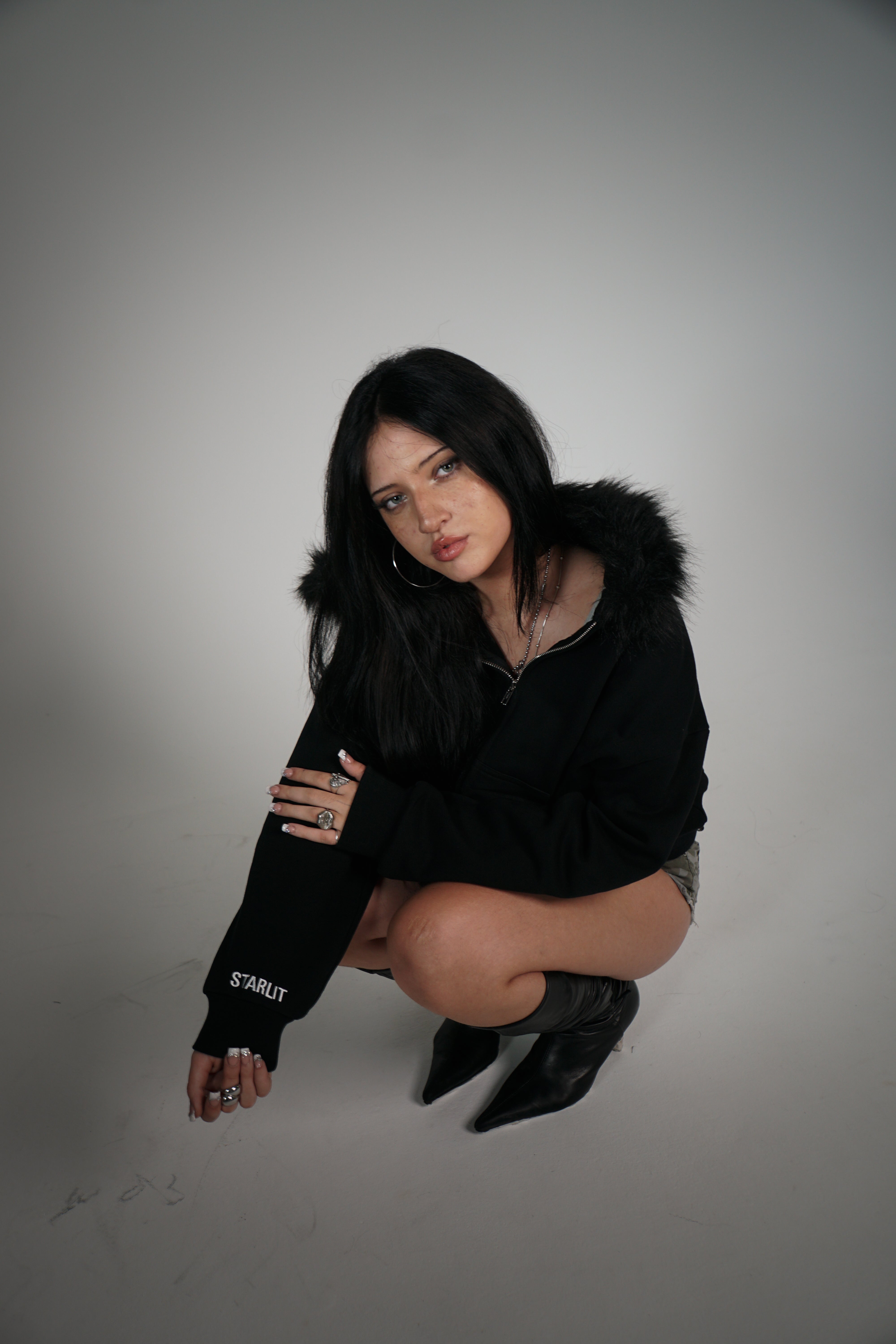 Woman wearing a black hoodie and boots on a plain background